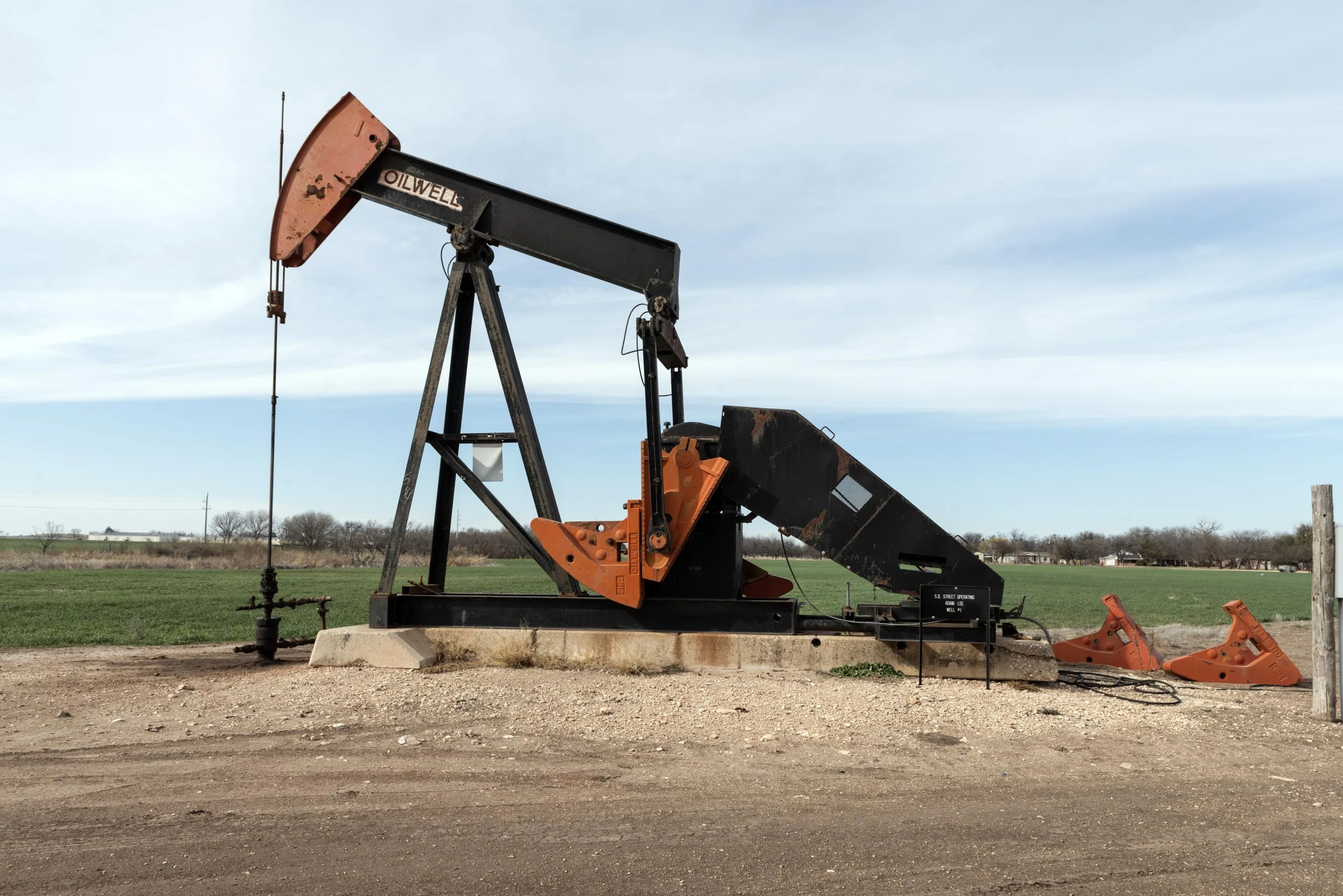An oil pumpjack, painted black and orange, working in a green field under a pale sky in West Texas.